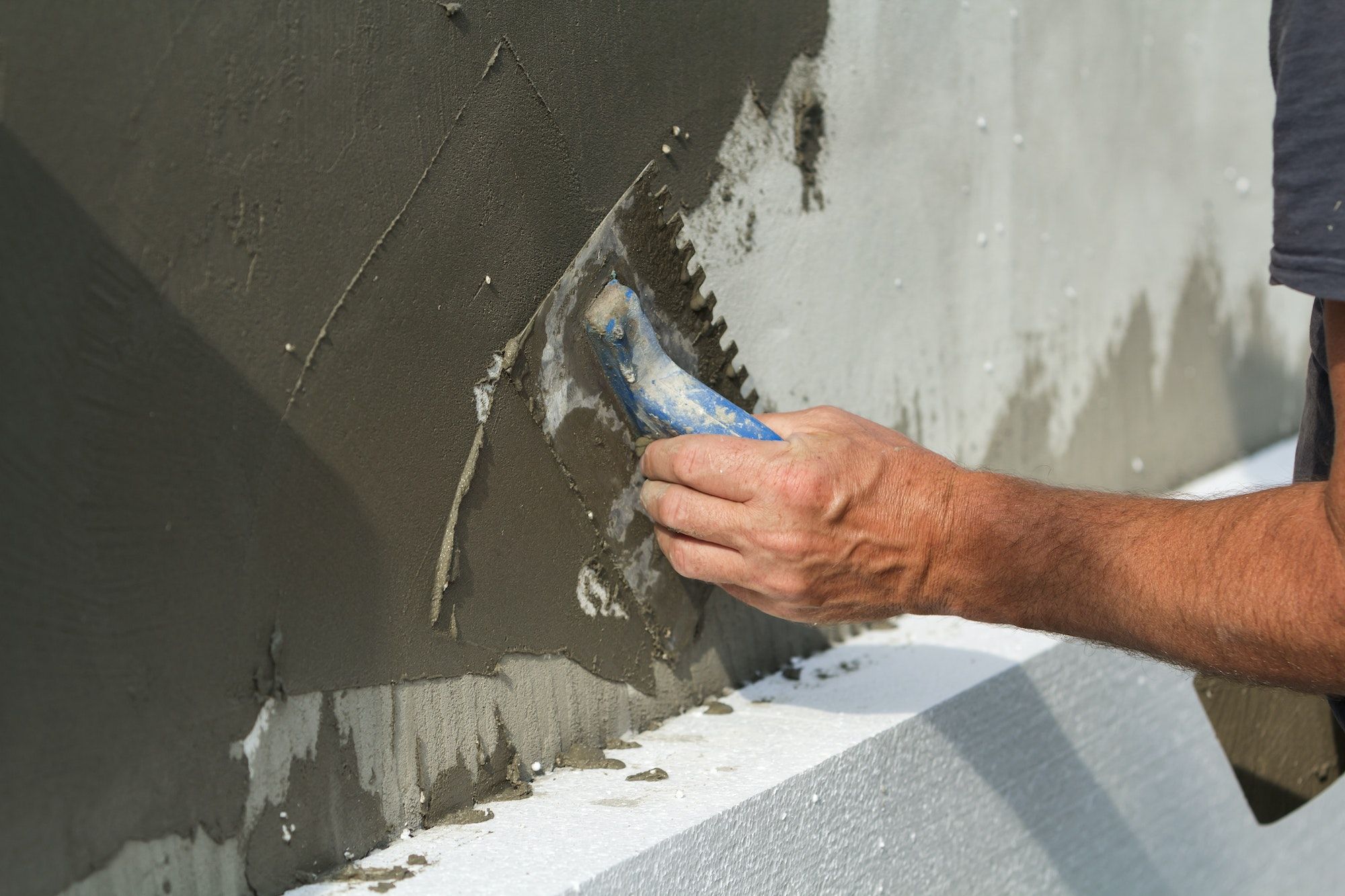 Close-up of detail of worker hand with trowel applying glue on plastered white house wall doing