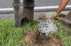 Worker installing a gravel-covered drain grate beside a black bucket catch basin near a curb